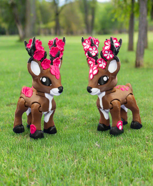 Two toy deer figures with floral antlers on a grassy field.
